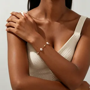Close-up of gold stainless steel bracelet with shell and pearl charms on model.