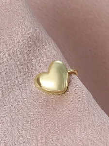 Close-up of a glossy gold heart-shaped ear cuff presented on pink textured fabric