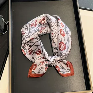 Foulard carré en soie à imprimé floral vintage noué en ruban sur plateau noir élégant.