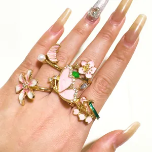 Vista detallada del juego de anillos dorados con flores y mariposas en esmalte rosa y cristales