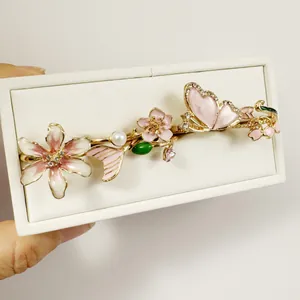 Primer plano de un pasador dorado con flores de esmalte rosa y una elegante mariposa