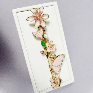 Vista detallada del pasador dorado con flores y mariposas de esmalte rosa y perlas