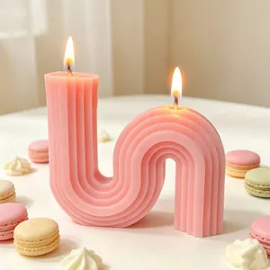 Close-up of a pink S-shaped geometric scented candle featuring two lit wicks and props
