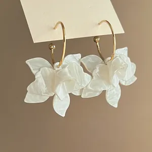 Primer plano de elegantes pendientes de aro con flores de resina blanca plisada.