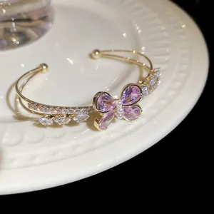 Detailed close-up of an elegant double-layered gold bracelet with a purple zircon butterfly