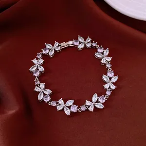 Close-up of silver flower bracelet with pink and clear zircon stones on brown fabric.