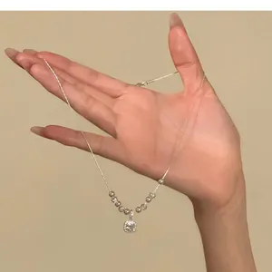 Detailed close-up of elegant silver necklace with square zircon pendant and pearls held on hand.