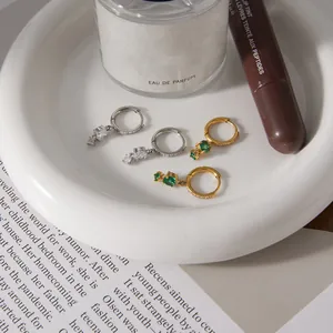 Dettaglio di orecchini a cerchio in acciaio inossidabile con ciondoli in zircone verde e bianco