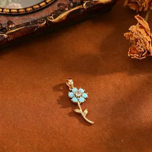 Detailansicht eines vergoldeten Blumenanhängers mit türkisfarbenen Blättern und Zirkon.