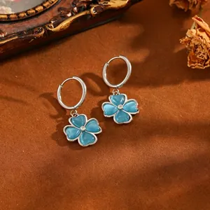 Detailaufnahme von silbernen Creolen mit blauen Katzenaugen-Glücksklee-Anhängern.