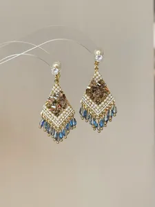Detail van vintage kwastjes oorbellen met bruine kristallen en blauwe kralen.