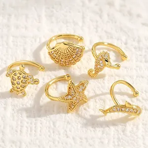 Detailed view of five gold ocean-themed ear cuffs with sparkling zirconia on white sand.