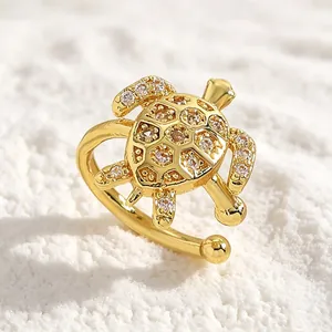 Detailed macro view of a gold turtle ear cuff with sparkling zircon on white sand