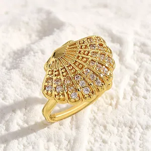 Close-up of a gold seashell ring with shimmering zircon stones on a white sand texture.