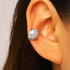 Close-up of a silver shell ear cuff with pavé zircons worn on the ear cartilage.