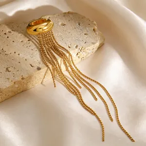 Macro view of a gold-plated stainless steel tassel ear cuff on beige stone backdrop
