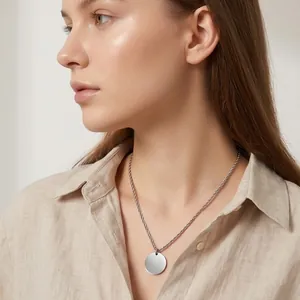 Detalle de un collar de acero inoxidable minimalista con colgante redondo en una modelo