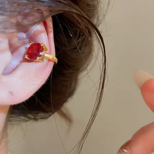 Λεπτομερής λήψη του κομψού επιχρυσωμένου ear cuff με κόκκινο ζιργκόν φορεμένο στο αυτί