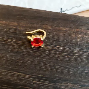 Κοντινό πλάνο χρυσού ear cuff με μια στρογγυλή κόκκινη πέτρα ζιργκόν