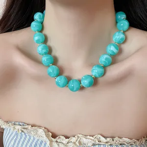 Detail view of a vibrant marbled turquoise acrylic round bead necklace worn by a female model.