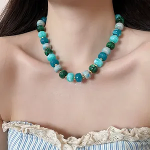 Détail d'un collier en perles d'acrylique marbrées vertes et bleues sur un mannequin.