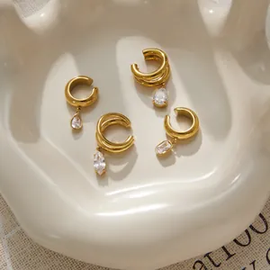 Elegant gold-plated stainless steel ear cuffs with sparkling zircon pendants on a cream dish.