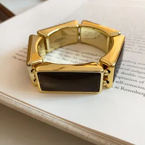 Dettaglio macro di un bracciale elastico rettangolare in resina dorata su un libro antico