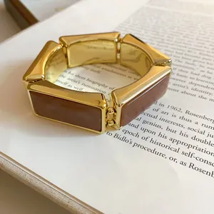Dettaglio del bracciale elastico vintage in resina dorata con maglie rettangolari su libro.