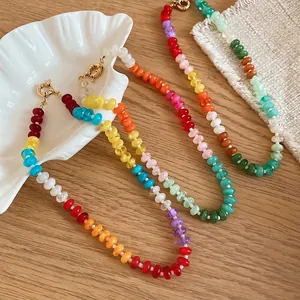 Colorful rainbow acrylic beaded choker necklace with gold clasp on wooden table with shell