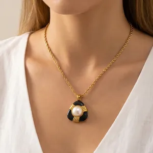 Gros plan d'un collier chaîne corde doré avec un pendentif en résine noire et perle