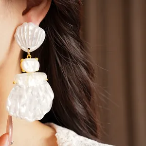Primo piano di eleganti orecchini a conchiglia in resina bianca con maglie dorate su una modella