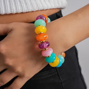 Close-up of colorful swirled acrylic beads with golden spacers on a model's wrist.