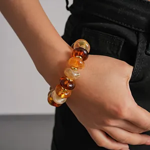 Close-up detail of retro amber acrylic marbled beaded bracelet worn on wrist with black denim