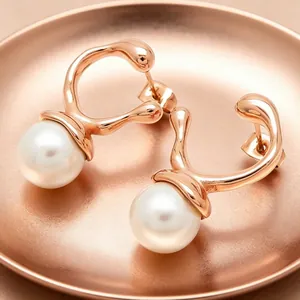 Detailed macro view of elegant rose gold irregular stud earrings with pearls on a matching tray