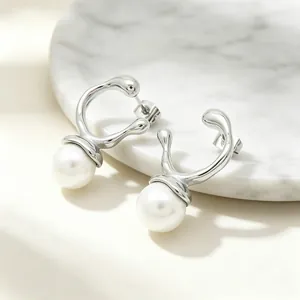 Close-up of irregular silver geometric earrings with large pearls on marble base