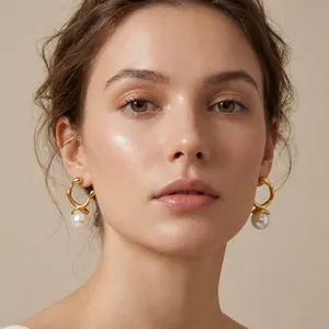 Elegant gold geometric earrings with white pearl drops worn by a female model in detail.