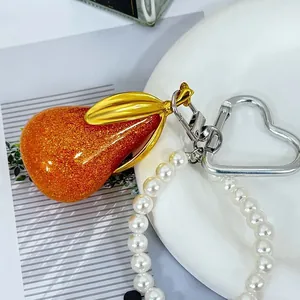 Detailopname van een peervormige harsbedel met oranje glitters en een parelkralenarmband