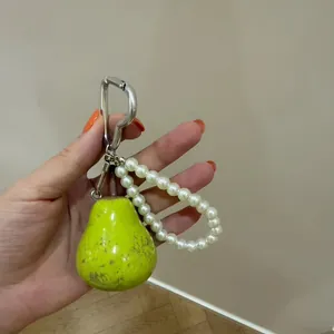 Gedetailleerd overzicht van een groene peren sleutelhanger van hars met parelband.