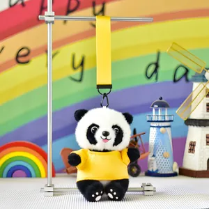 Close-up of a cute panda plush keychain with yellow t-shirt hanging on metal display stand