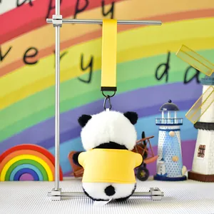 Back view of cute panda plush keychain wearing a yellow coat, hanging on a metal stand.