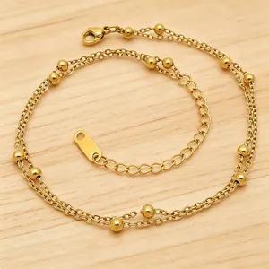 Nahaufnahme eines zweilagigen Edelstahl-Fußkettchens mit Goldperlen und verstellbarem Verschluss.