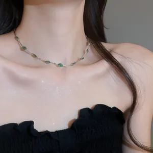 Close-up van een delicate zilveren ketting met groene bladhangers om de hals van een model