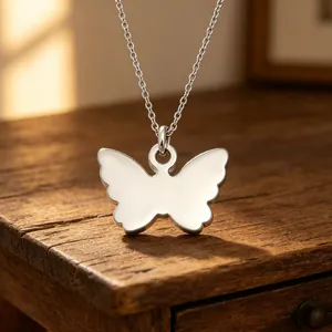 Detail shot of a minimalist silver butterfly pendant with mirror finish on wood
