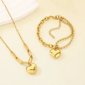 Nahaufnahme eines goldenen Herzanhängers an einem doppellagigen Armband und einer Halskette