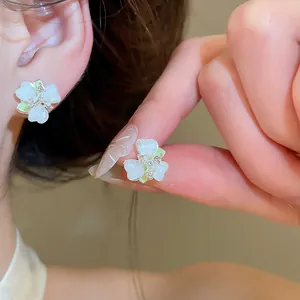 Detailed macro view of white flower stud earrings with green accents and inlaid stones