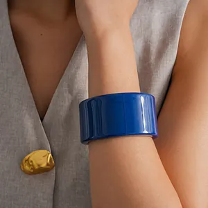 Detailansicht eines breiten, glänzend blauen Armreifs am Arm eines Modells mit Weste