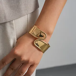 Nahaufnahme eines goldenen, unregelmäßigen geometrischen Cross-Over-Armreifs am Handgelenk.
