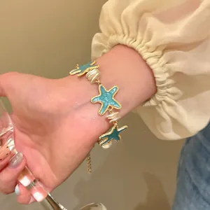 Detailed view of women's mint green enamel starfish bracelet with pearls on a wrist