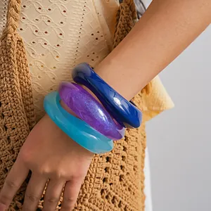Close-up detail of three colorful chunky resin bangles styled with a woven straw bag