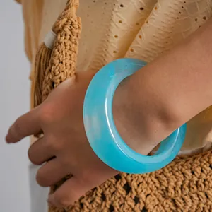 Close-up detail of a chunky cyan marbled resin bangle styled with a woven straw bag